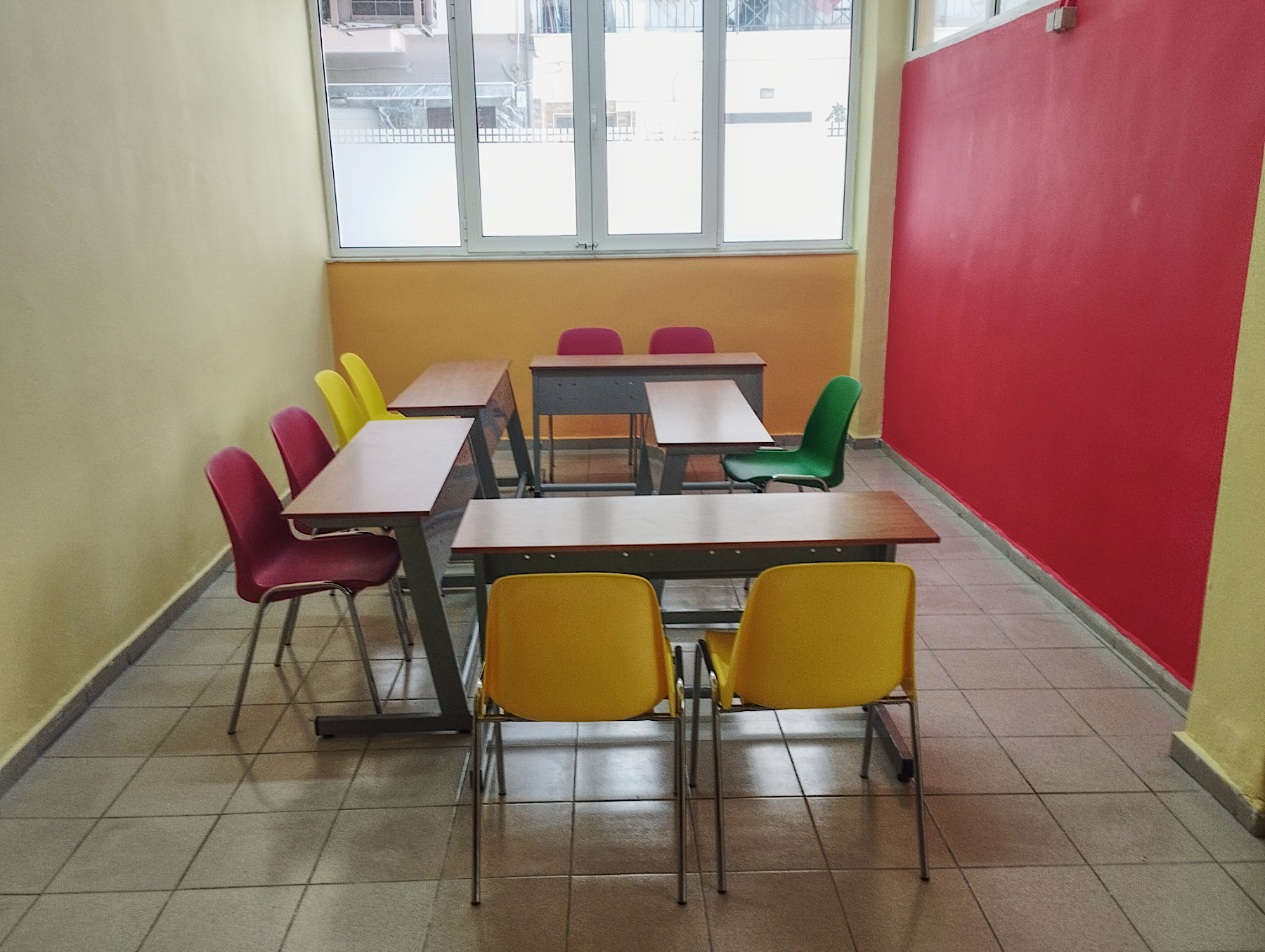 Αίθουσα διδασκαλίας με κόκκινο πίνακα και οργανωμένα θρανία.