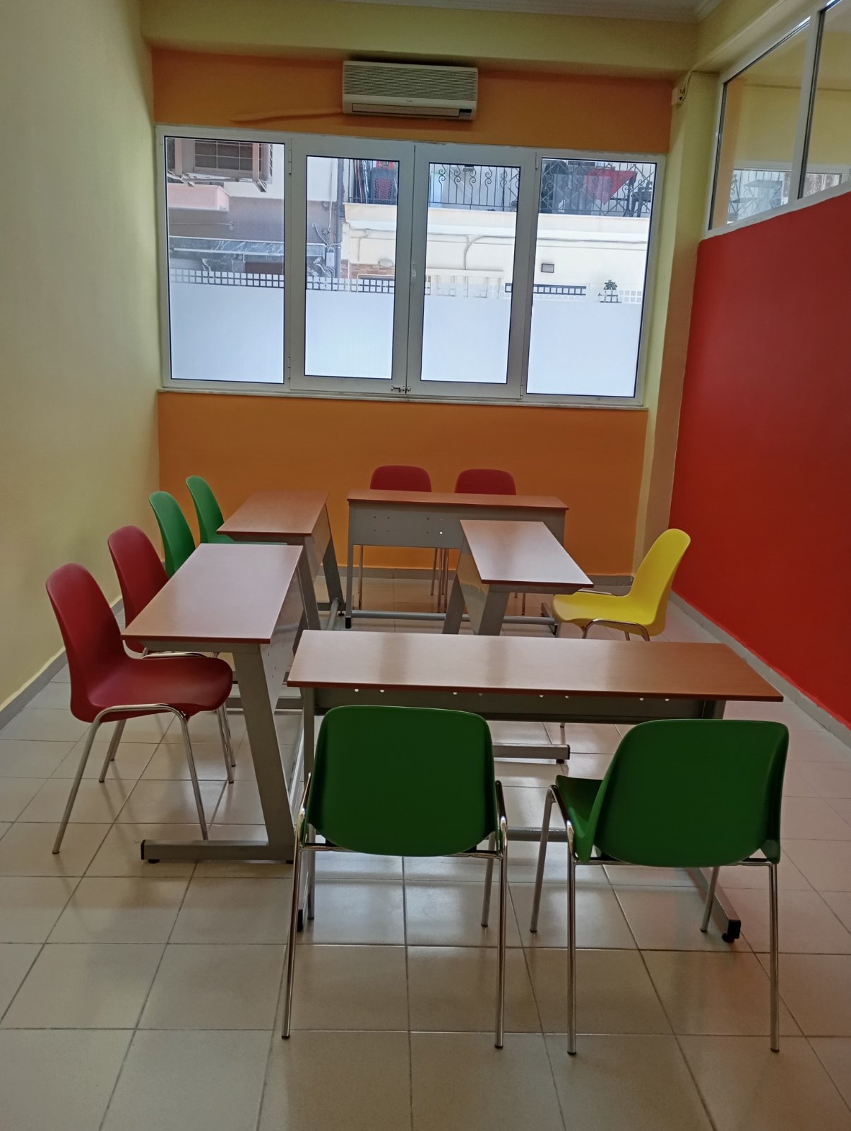 Αίθουσα Thess English με θρανία και πολύχρωμες καρέκλες.