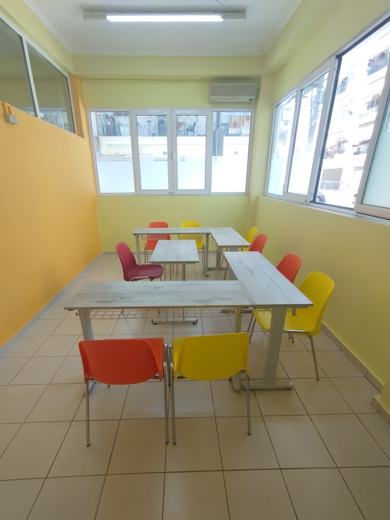 Φωτεινή αίθουσα Thess English με θρανία σε διάταξη ομάδας.